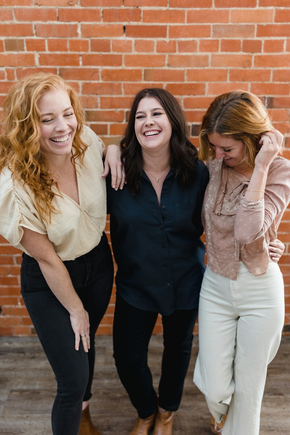 three women standing next to each other in front of a brick wall