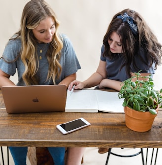 two girls sitting at a table with a laptop