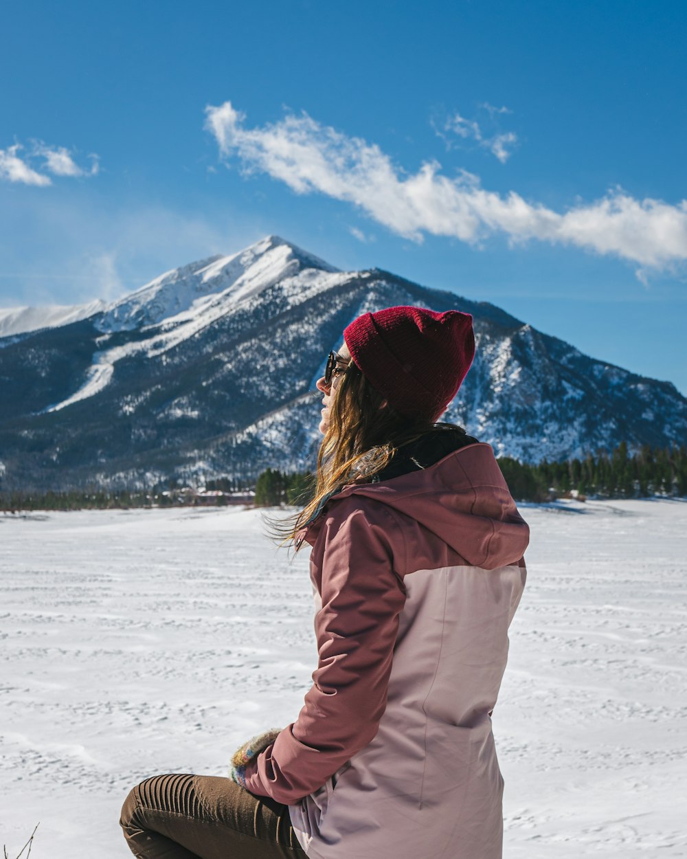 a woman sitting in the snow with a mountain in the background