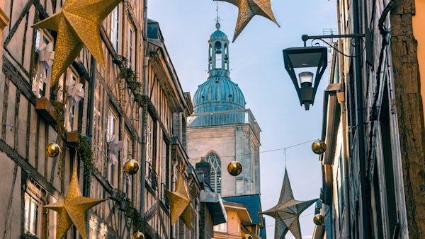 A half-timbered street with Christmas stars and a tower beyond — Rouen, France