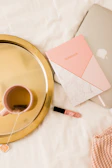 Flat lay of a laptop, notebook, and a cup of tea on a white desk with a pink accent