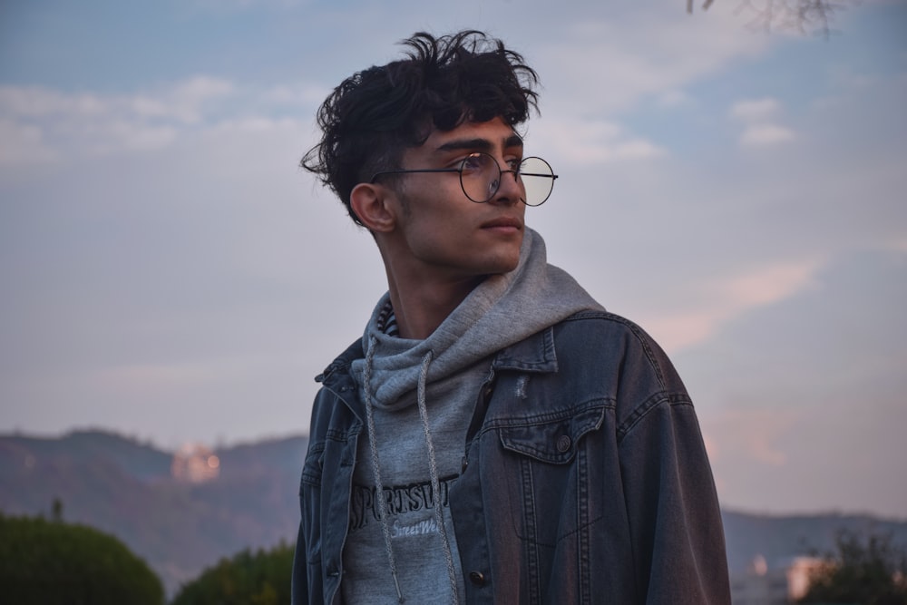 a man wearing glasses and a hoodie looks off into the distance