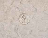 A coin with a profile of a man in a suit, surrounded by text. The background consists of a sandy or textured surface.