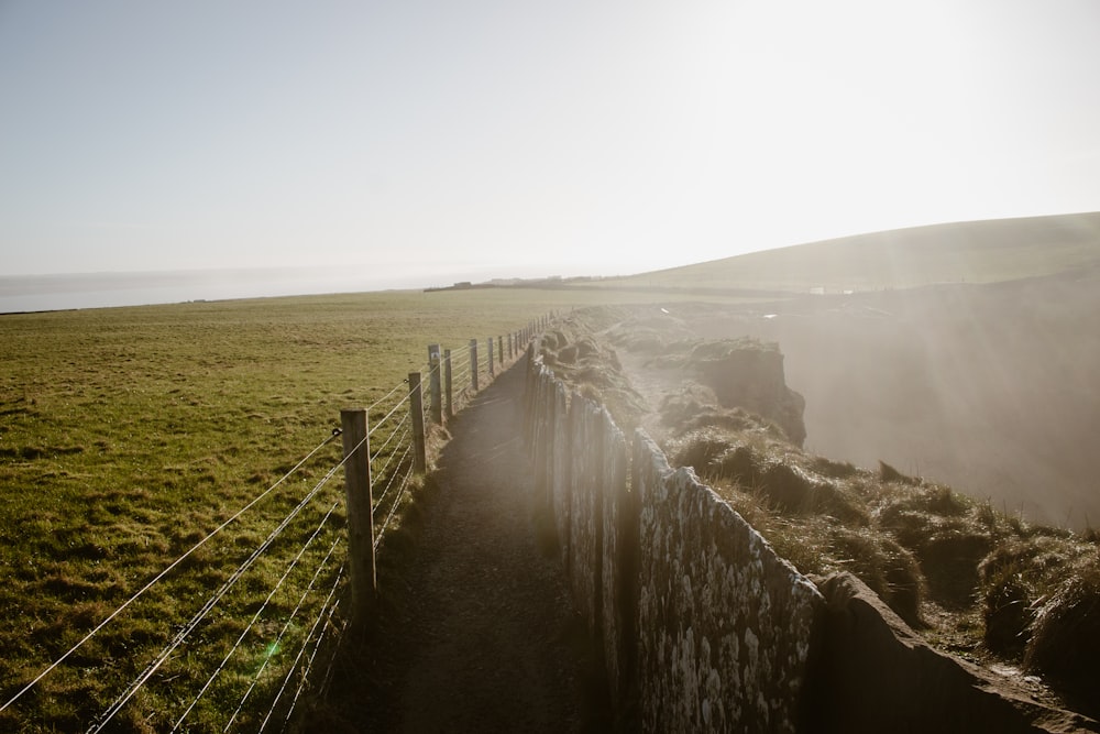 a grassy field with a fence and a grassy hill in the background