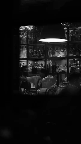 Shadowy bar scene featuring a bartender preparing a drink, with dark forest green backdrop and rich gold highlights.
