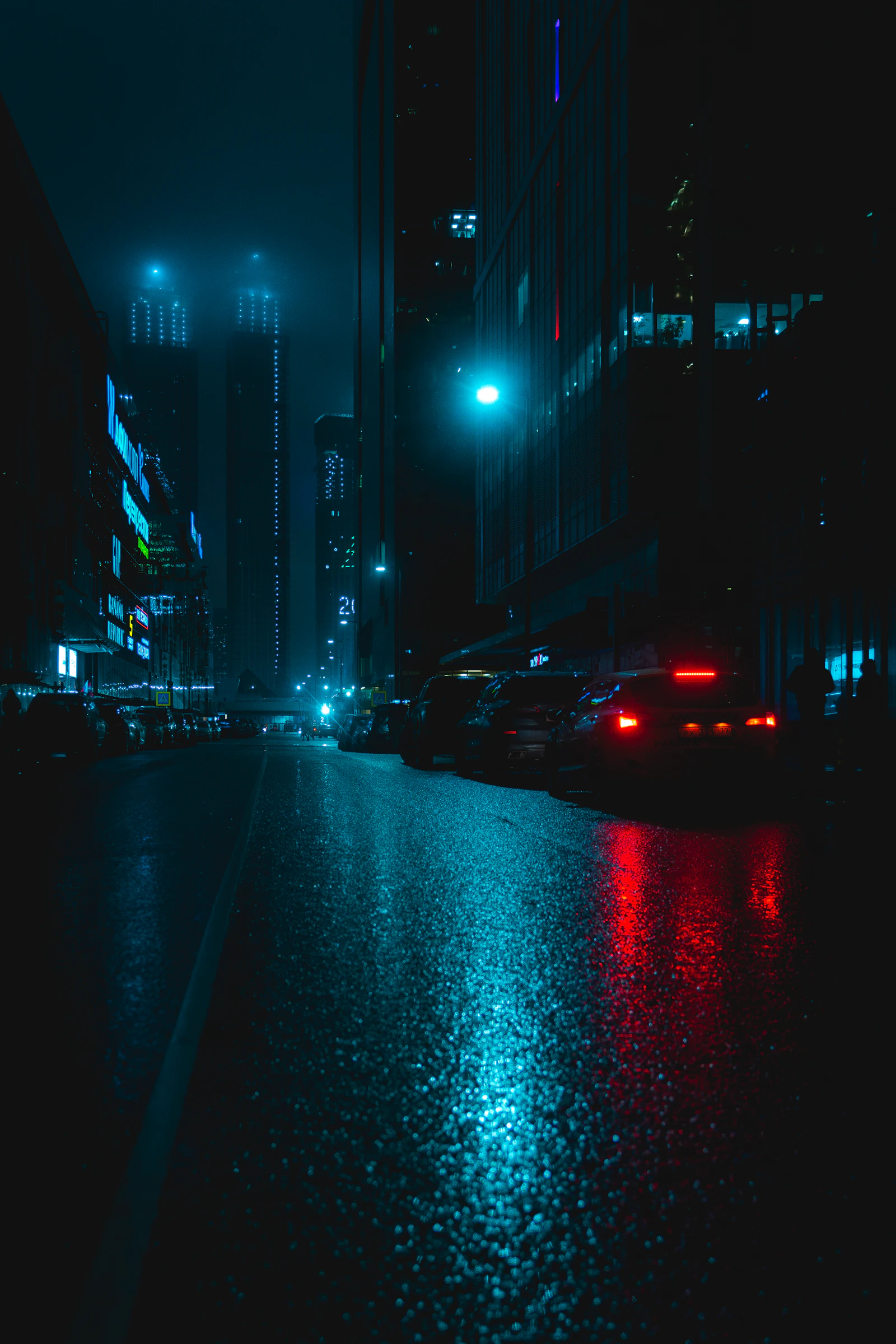 A city street at night with cars parked along the side of the road