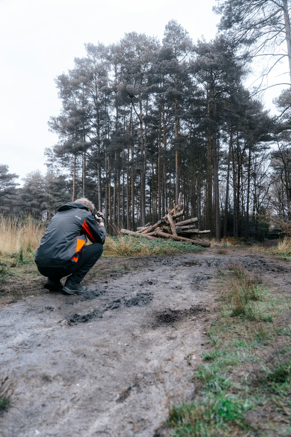 a man kneeling down on a dirt road in front of a forest