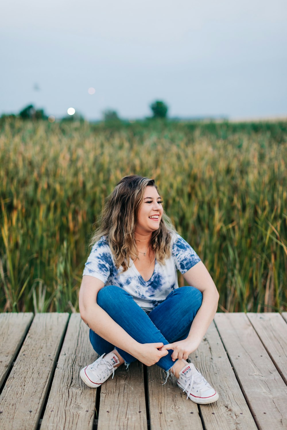 uma mulher sentada em um deck de madeira na frente de um campo de milho