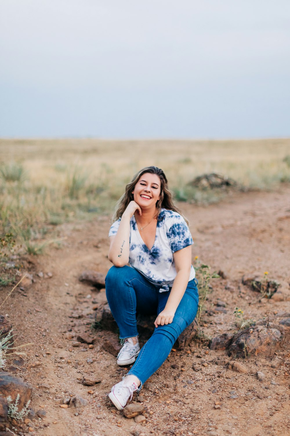 a woman sitting on a dirt road in the middle of a field