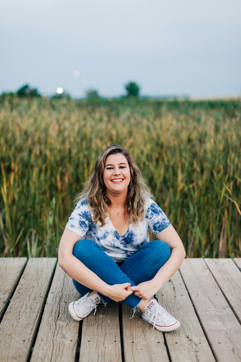 a woman sitting on a wooden deck in front of a field