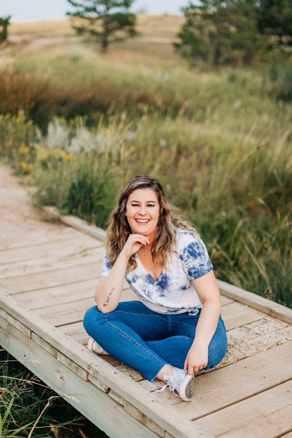 a woman sitting on a wooden bridge in a field