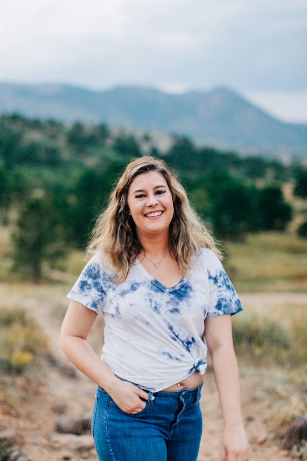 a woman standing on a dirt road in front of mountains