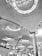 The architectural design features a modern ceiling with an intricate pattern of lines and illuminated circular light fixtures. Large columns support the ceiling, and below, there are signs above counters indicating check-in areas or ticketing services.