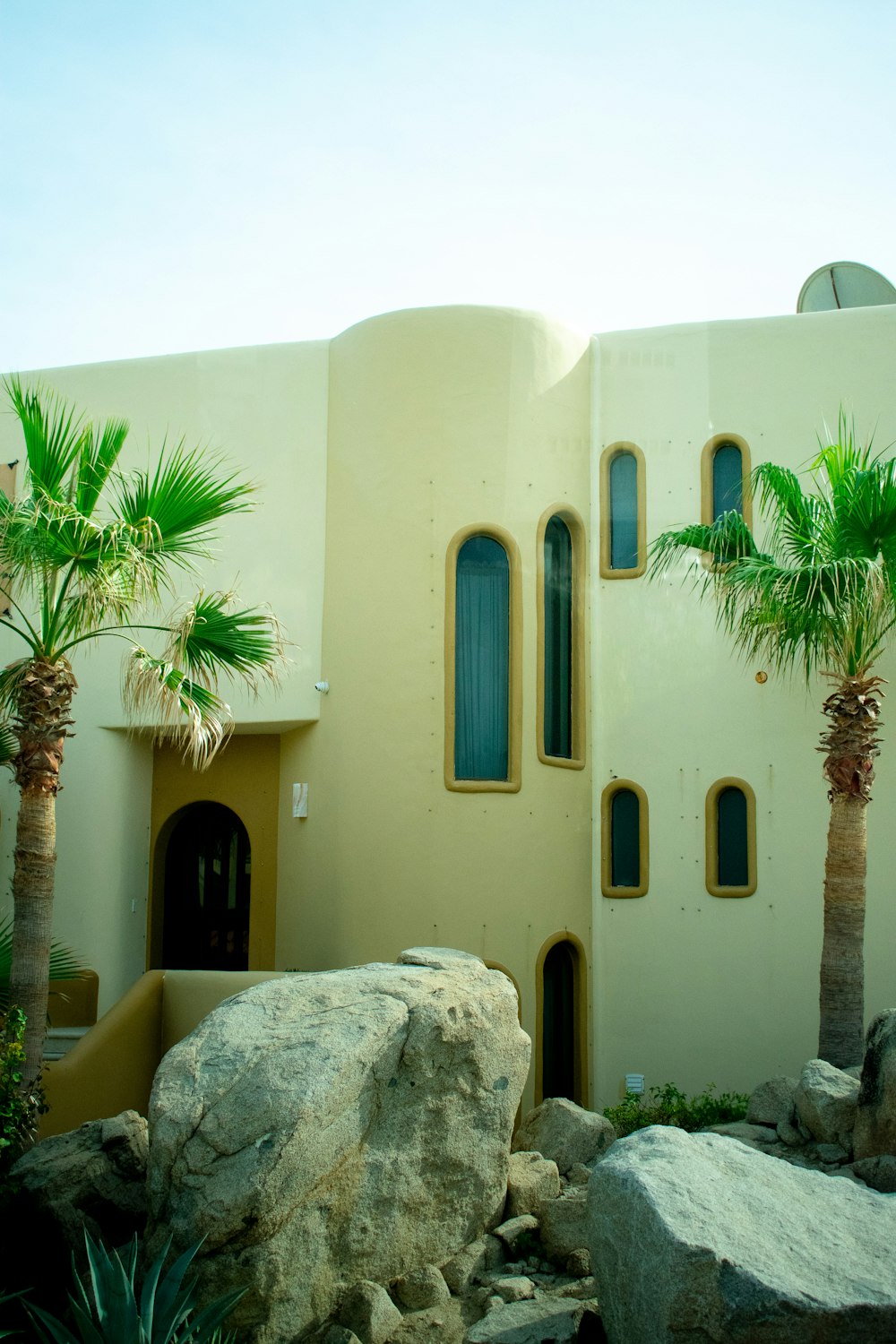 a white building with palm trees and rocks in front of it
