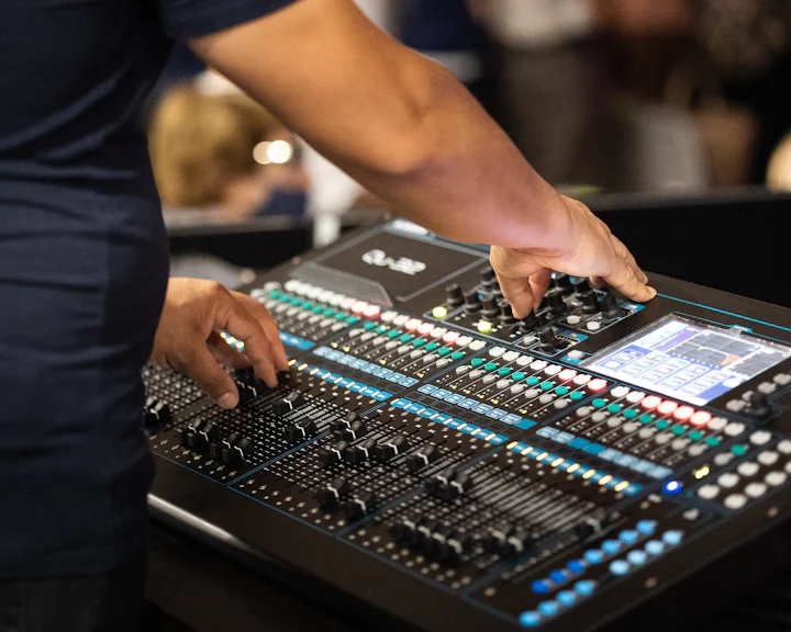 A person operating a sound and lighting control desk.