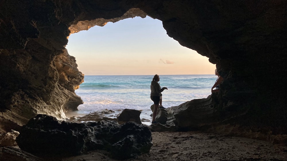 uma pessoa de pé em uma caverna olhando para o oceano