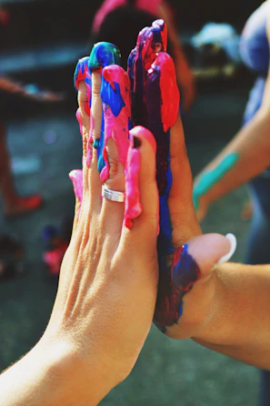 Close-up of hands working together on a creative art project with vibrant paints and brushes.