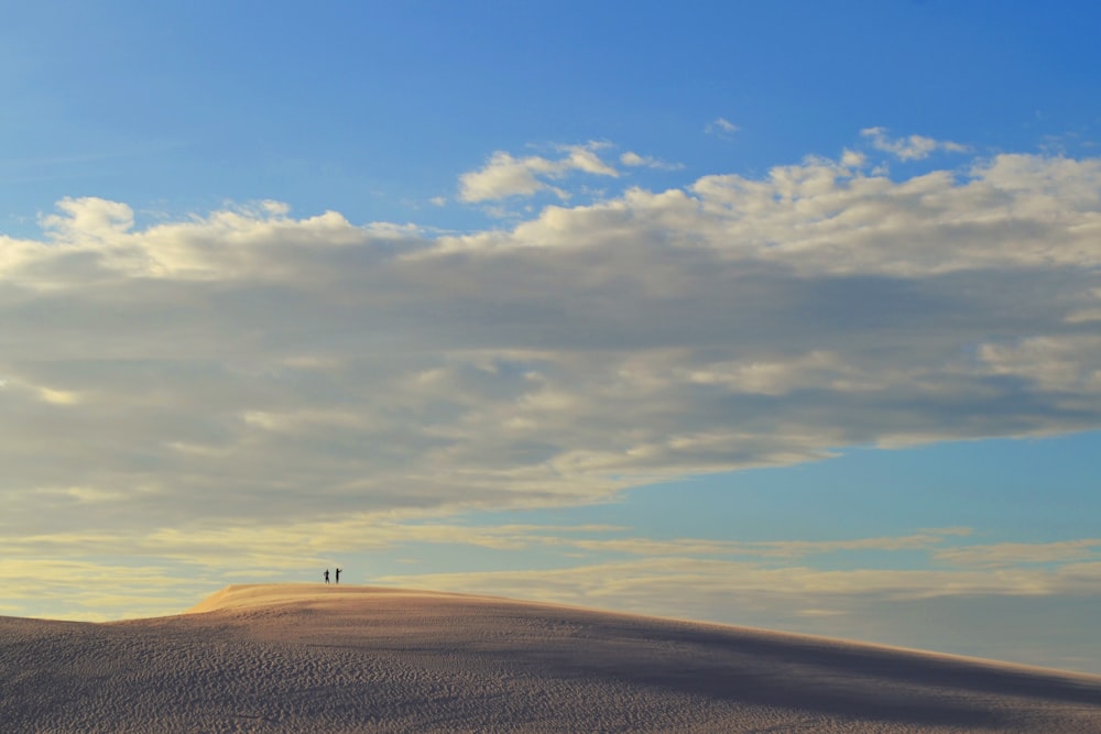 two people standing on top of a hill under a cloudy sky