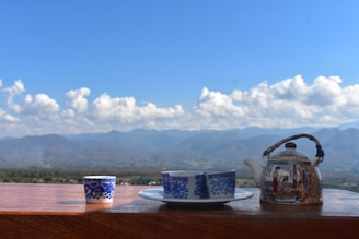 a tea pot and a cup on a table with mountains in the background