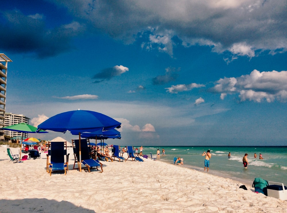 a beach filled with lots of people under blue umbrellas