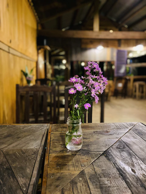 A rustic wooden table displaying colorful flower bouquets in mason jars under a soft sunset glow
