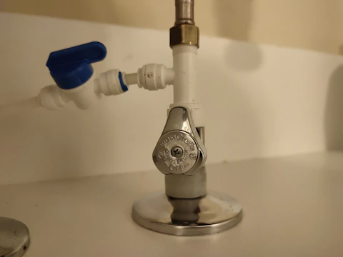 A close-up view of plumbing components including a shut-off valve with a metallic handle labeled 'OFF' on a pipe, adjacent to a blue-handled plastic valve.