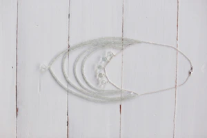 Delicate silver necklaces with sparkling stones arranged artistically on a white marble slab