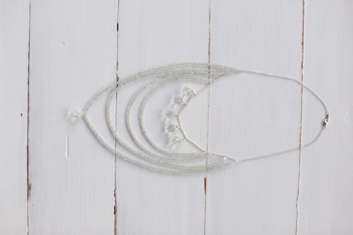 Delicate silver necklaces with sparkling stones arranged artistically on a white marble slab