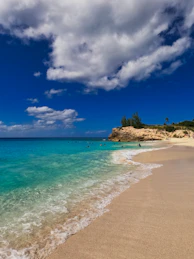 a sandy beach with clear blue water under a cloudy sky