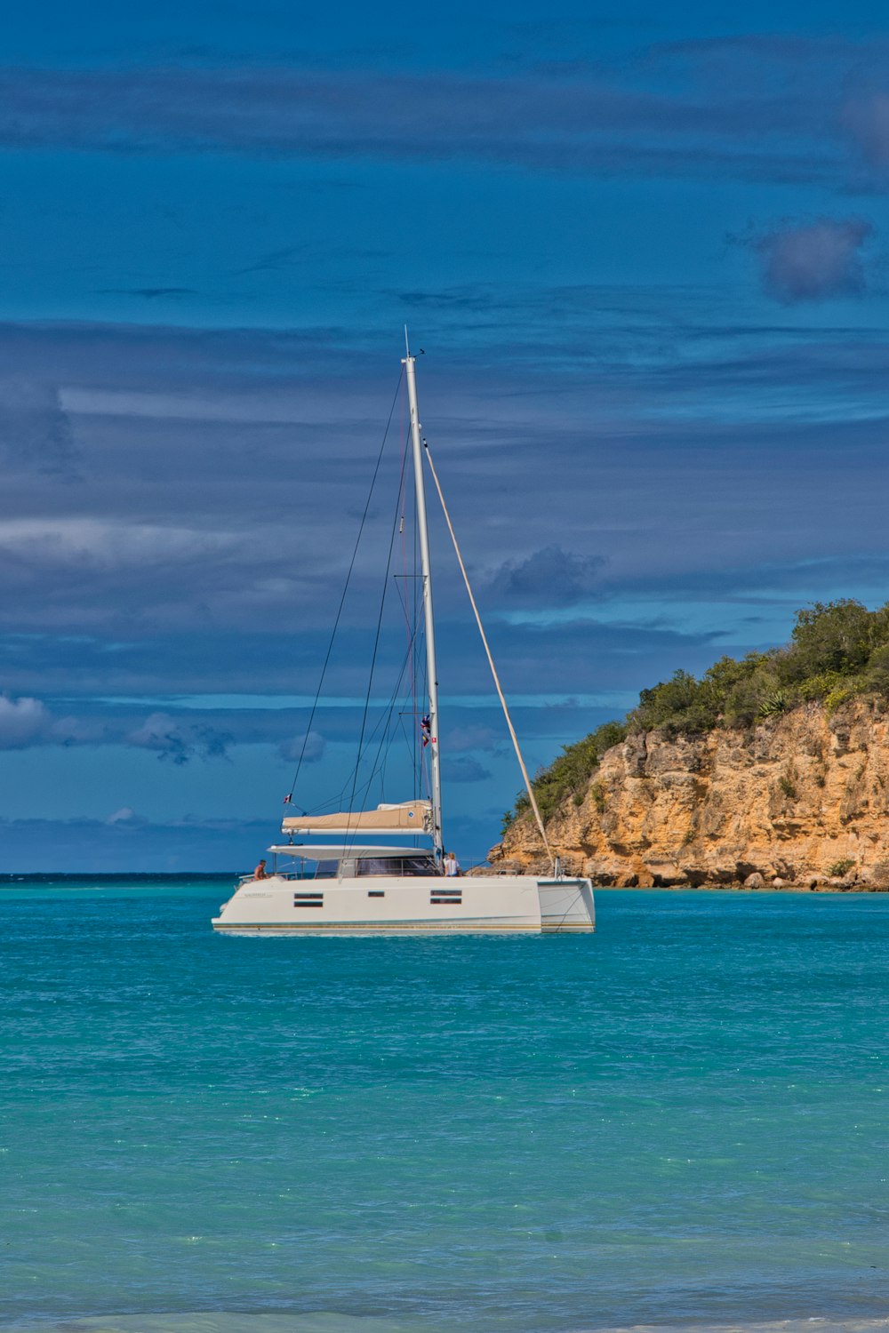 a sailboat floating in the ocean near a rocky shore