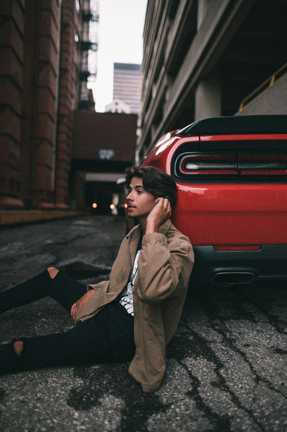 a man sitting on the ground next to a red car