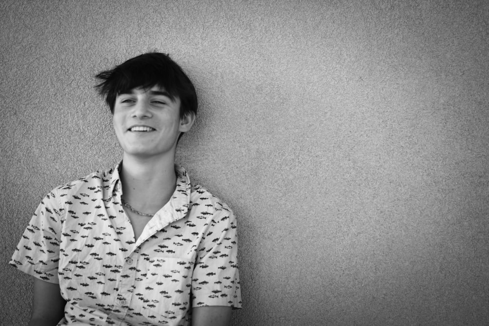 a young man is smiling while sitting against a wall