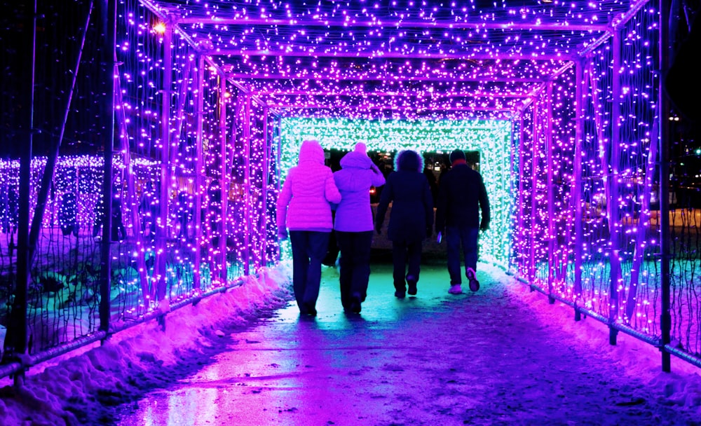 a group of people walking through a tunnel covered in purple lights