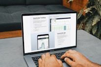 A person is using a MacBook Pro, viewing financial trading information from Questrade. The screen displays detailed trading data and an app interface, emphasizing connectivity and accessibility. The image features a modern setting with a couch in the background and some houseplants.