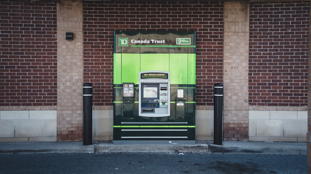 a green and black atm machine in front of a brick building