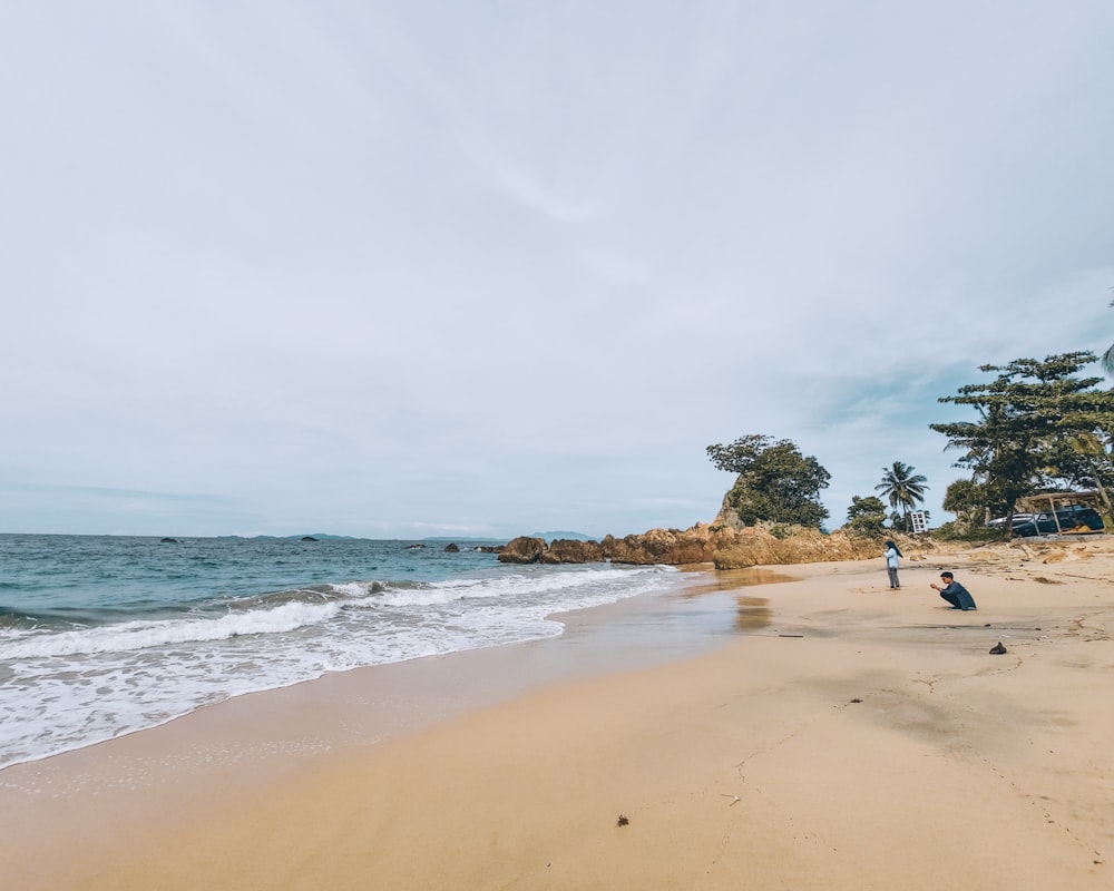 a couple of people standing on top of a sandy beach