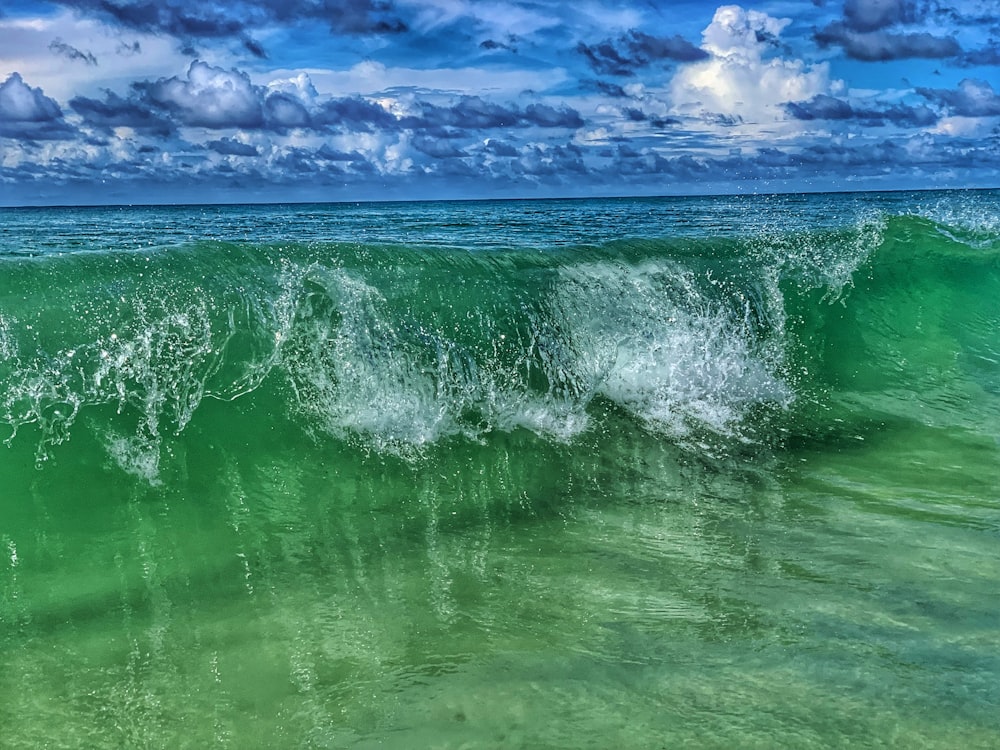 a green ocean wave with a blue sky in the background