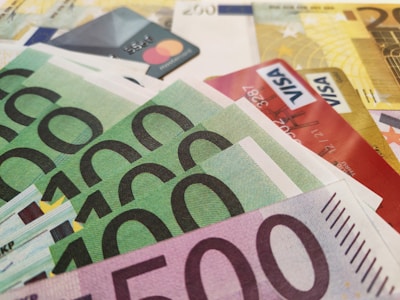 A close-up view of various Euro banknotes and credit cards scattered together. The banknotes have denominations of 500 and 100 Euros, while the visible credit cards include both Mastercard and Visa. The composition suggests a theme related to finance and currency.
