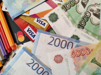 A scattered arrangement of various banknotes and credit cards, including Visa and Mastercard. The banknotes are in denominations of 1000, 2000, and 5000, featuring different colors and designs.