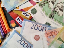 A scattered arrangement of various banknotes and credit cards, including Visa and Mastercard. The banknotes are in denominations of 1000, 2000, and 5000, featuring different colors and designs.