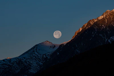 a full moon rising over a mountain range