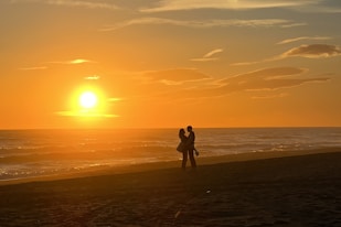 a couple of people standing on top of a sandy beach