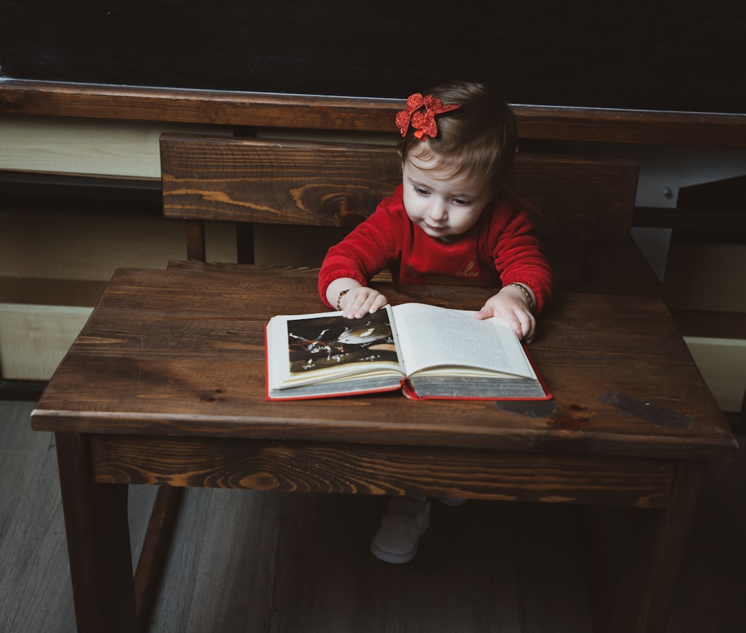 a little girl sitting at a table reading a book,
