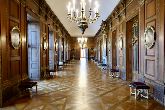 A warmly lit hallway in the mansion with period wallpaper and antique light fixtures.