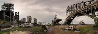 A post-apocalyptic scene featuring dilapidated buildings, a broken bridge covered with vegetation, and an abandoned car. The landscape is barren with scattered debris, suggesting an urban area left in ruins.