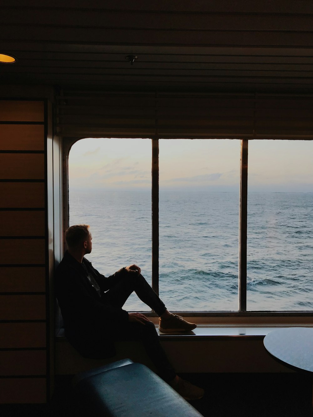 a man sitting on a window sill looking out at the ocean