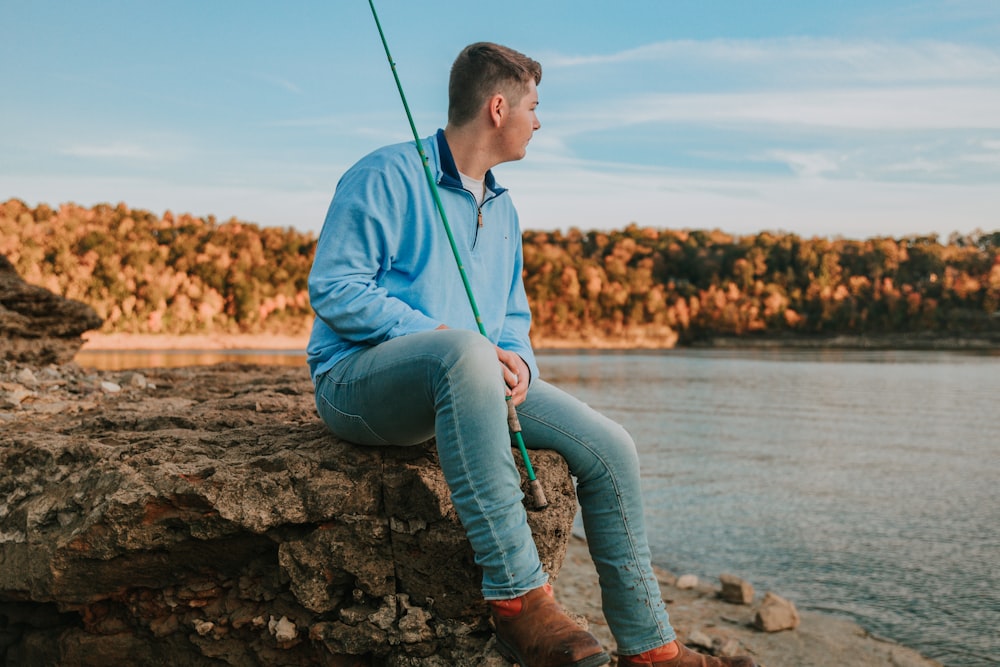 a man sitting on top of a rock next to a body of water