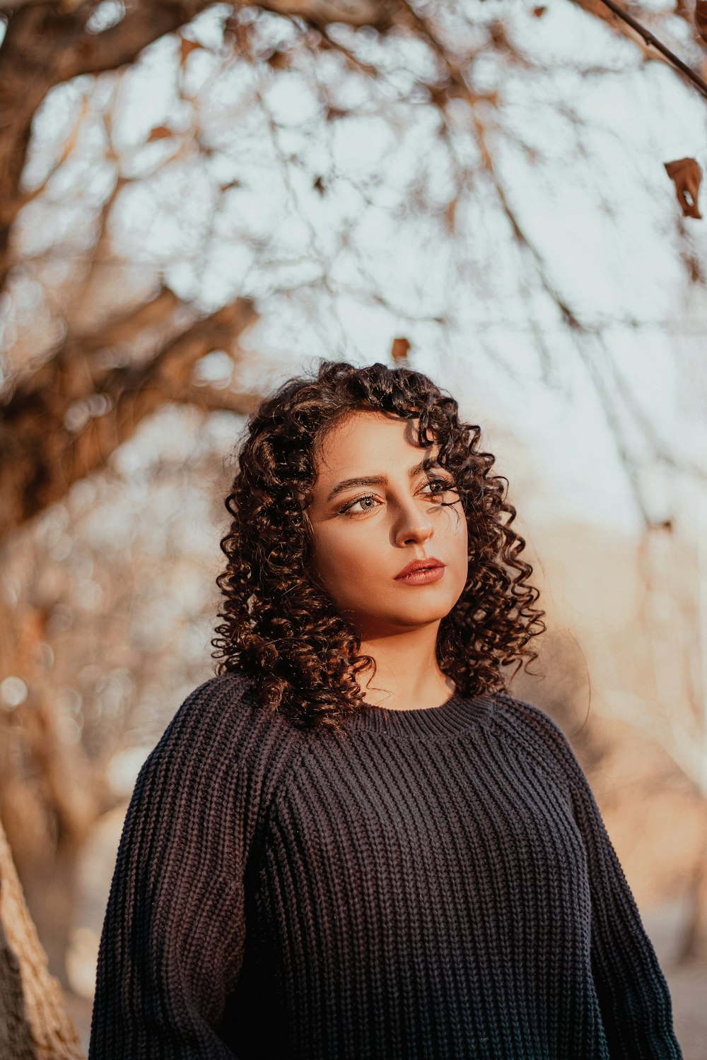 a woman with curly hair standing in front of a tree