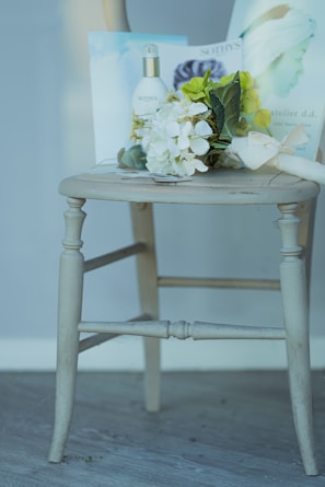 A wooden chair displaying a bouquet of white and green flowers, a bottle labeled 'Sothys', and some printed materials placed on its seat.