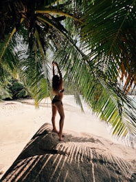 a woman in a bikini standing on a beach under a palm tree